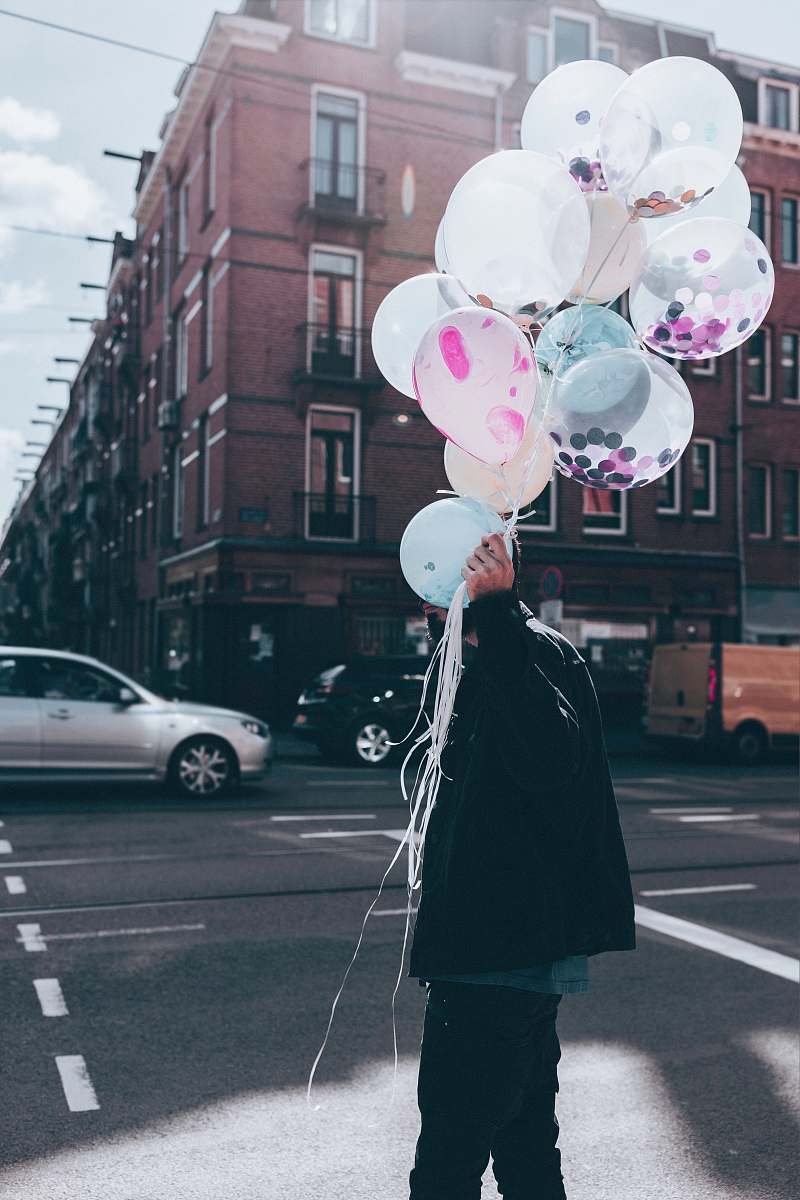 person man holding white balloon walking on street during day time people