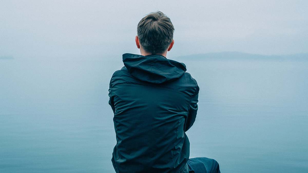 people man in black hoodie sitting in front of ocean person
