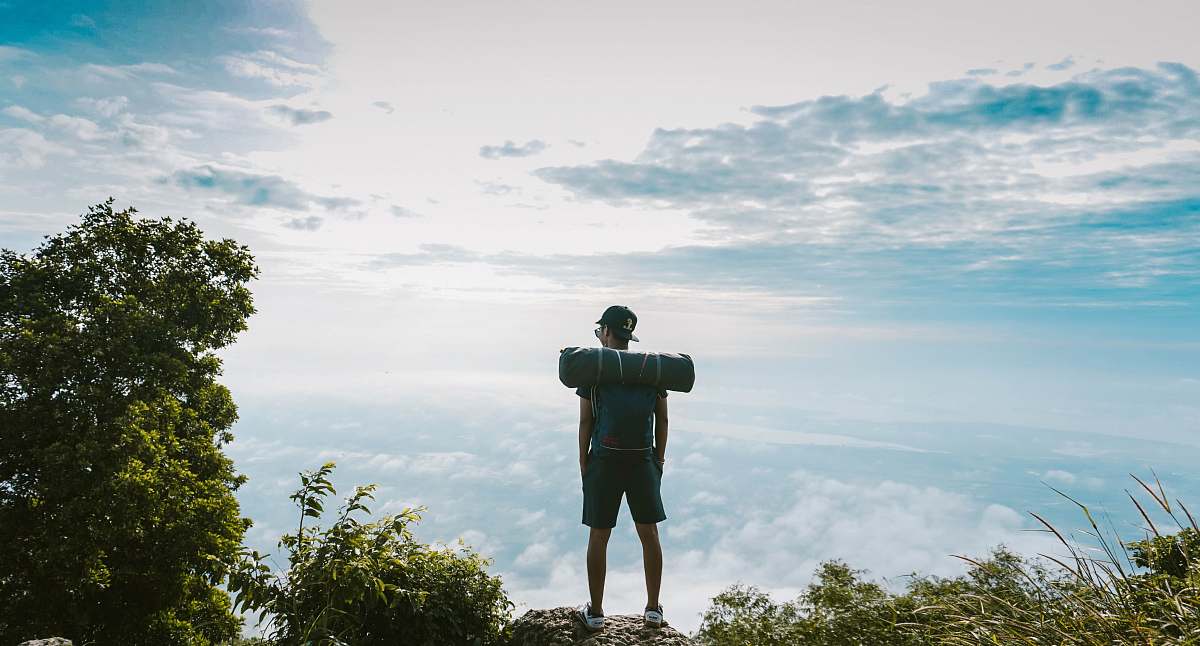 person man in black shirt standing on cliff facing sea of clouds people