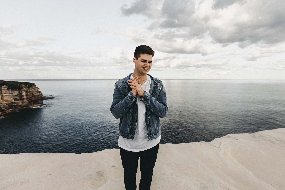 people man in blue denim jacket standing on cliff near body of water person