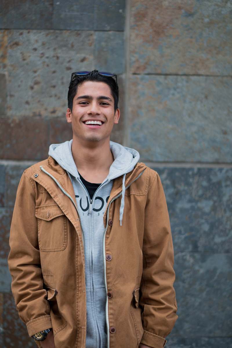 people man in brown coat standing near concrete wall smiles person