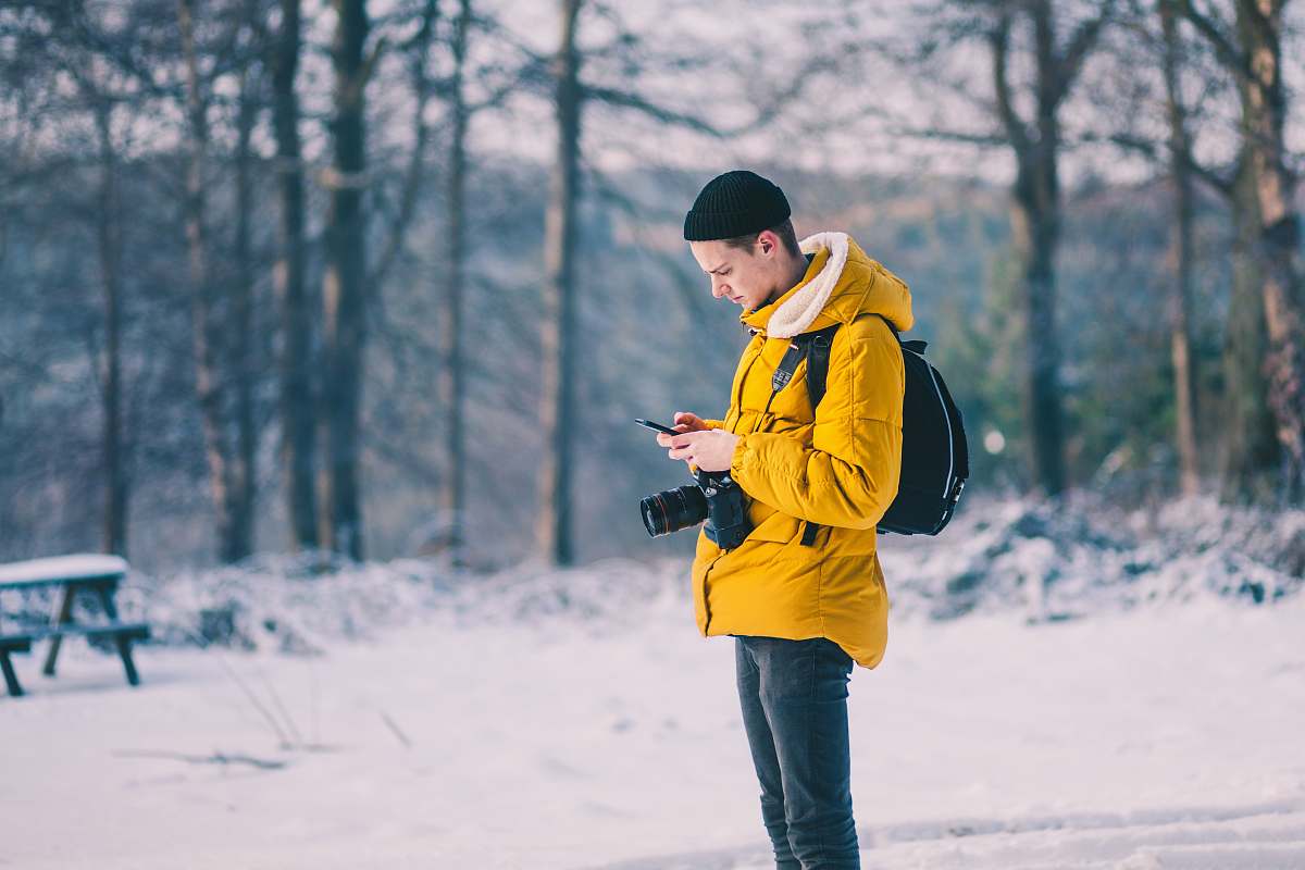 person man in brown jacket using his smartphone bench
