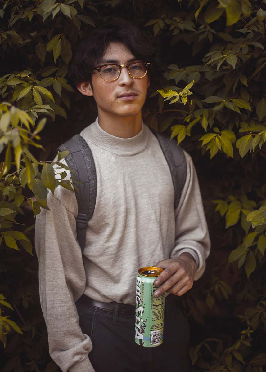 people man in gray sweatshirt holding can standing near leaves person