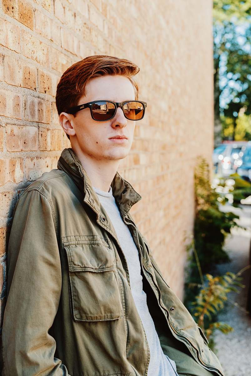people man in green jacket leaning on brown brick wall person