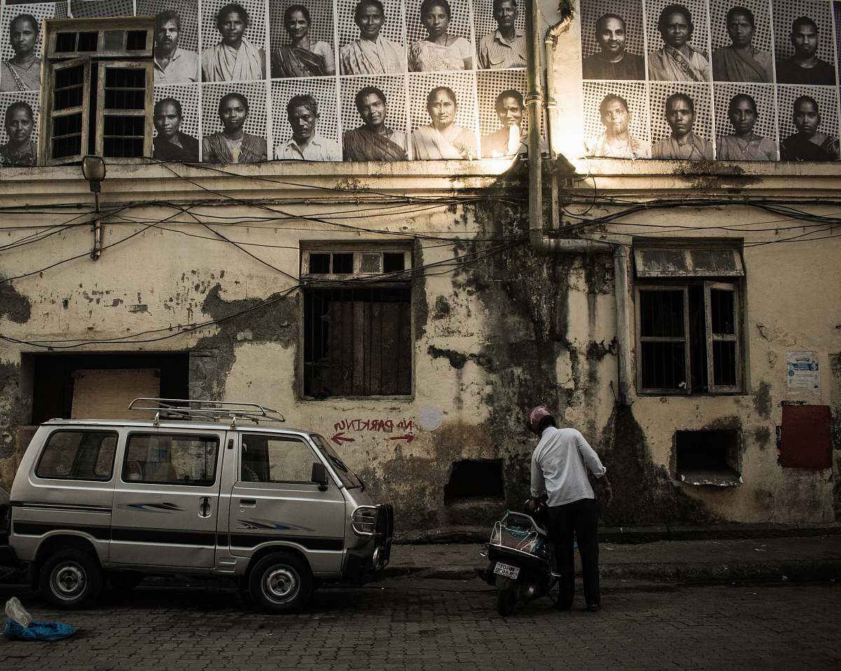 people man in white shirt beside black motor scooter looking up at sketch portraits hanged on building wall person