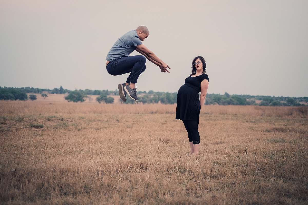 people man jumping in front of woman standing on field person