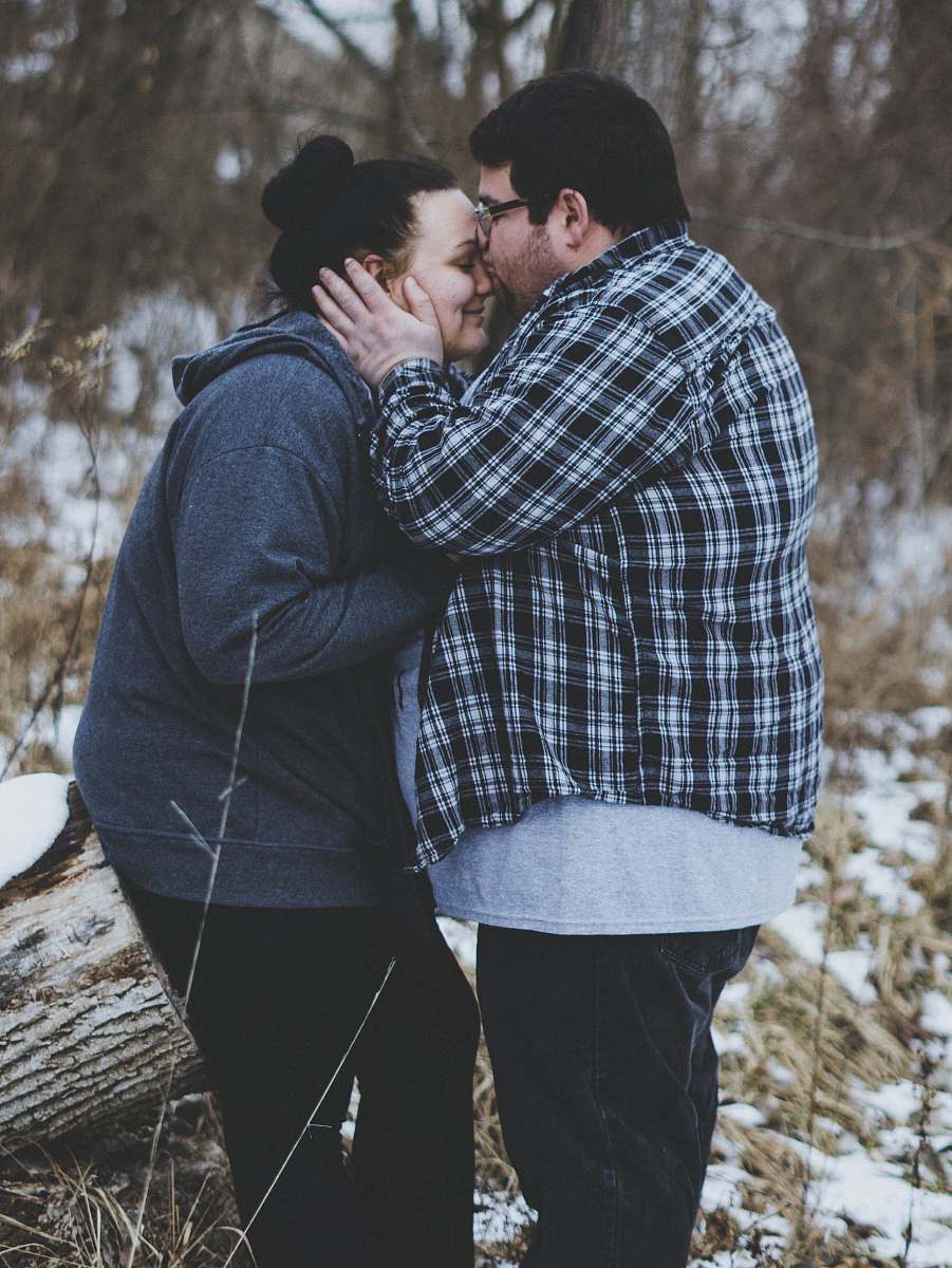 people man kissing woman while standing near trees during daytime person
