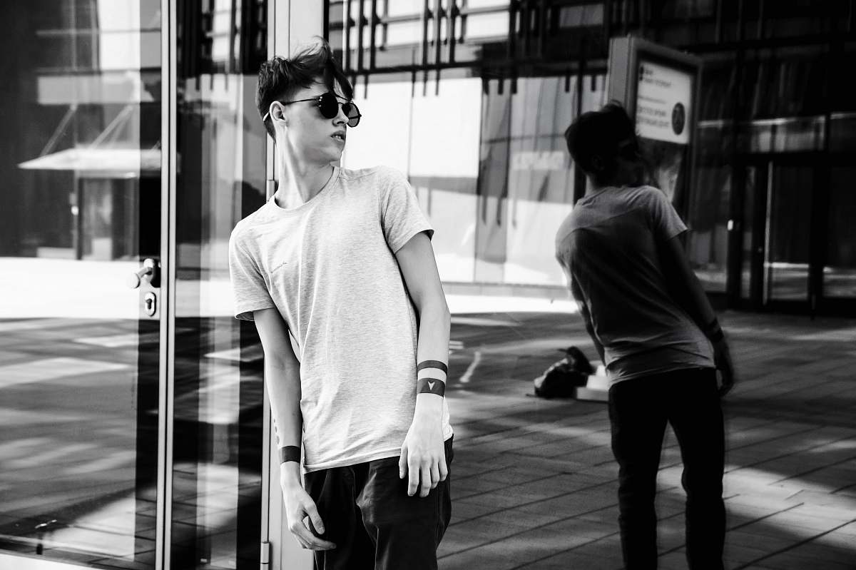 person man leaning on glass wall while looking on his right side black-and-white