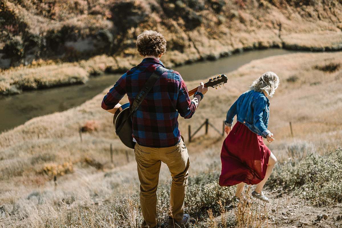 people man playing guitar standing behind woman on mountain person