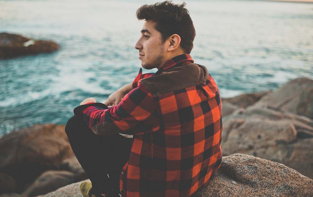 people man sitting boulder near body of water sea