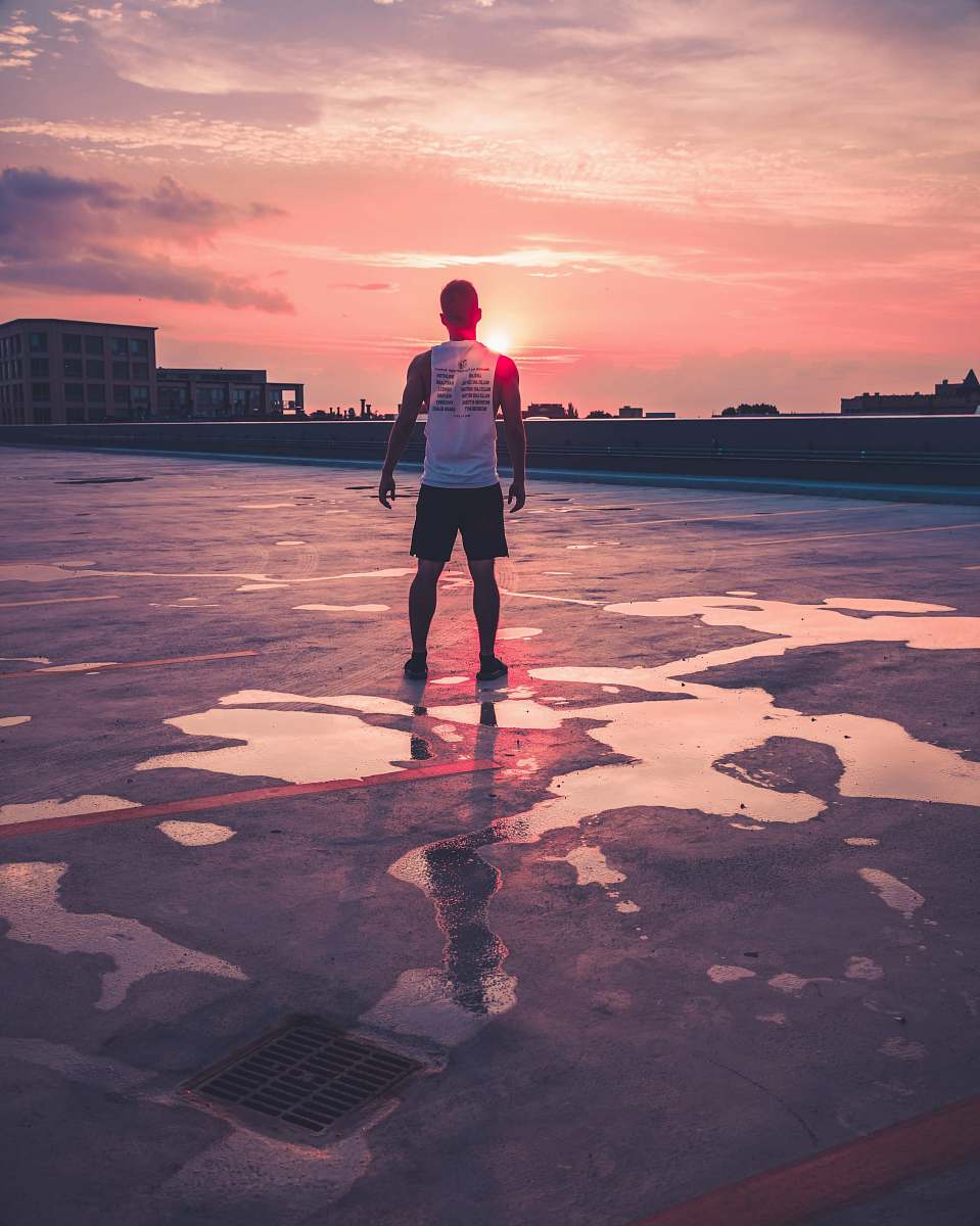 people man standing above gray concrete area facing large buildings at golden hour person