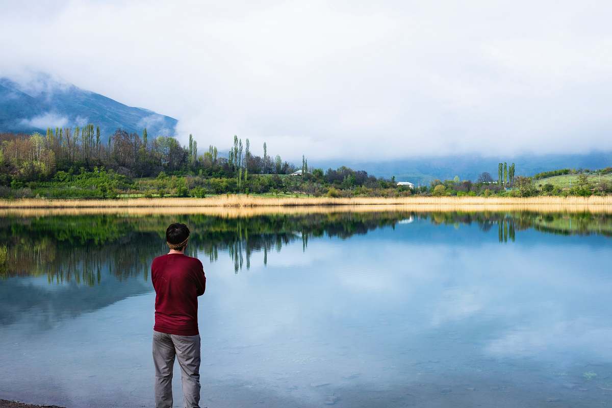 people man standing near body of water and trees person