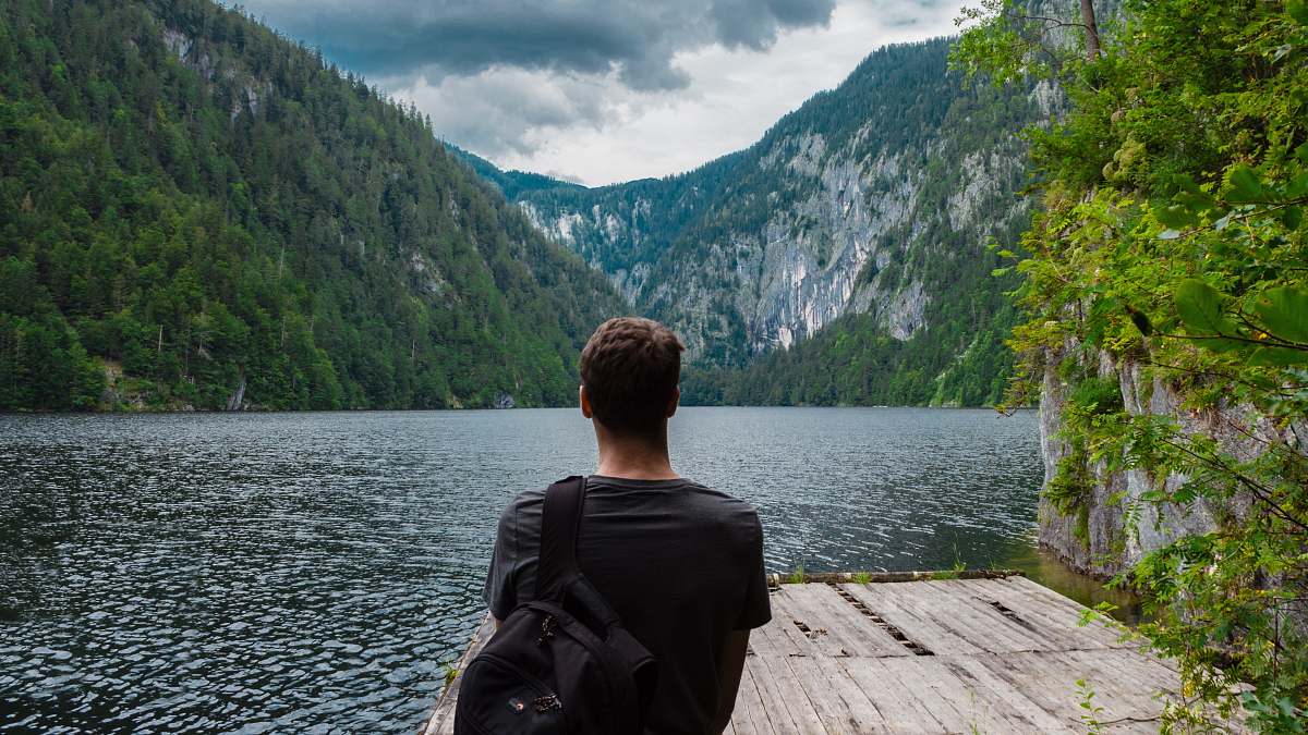 people man standing on brown wooden board near body of water surrounded by mountains back
