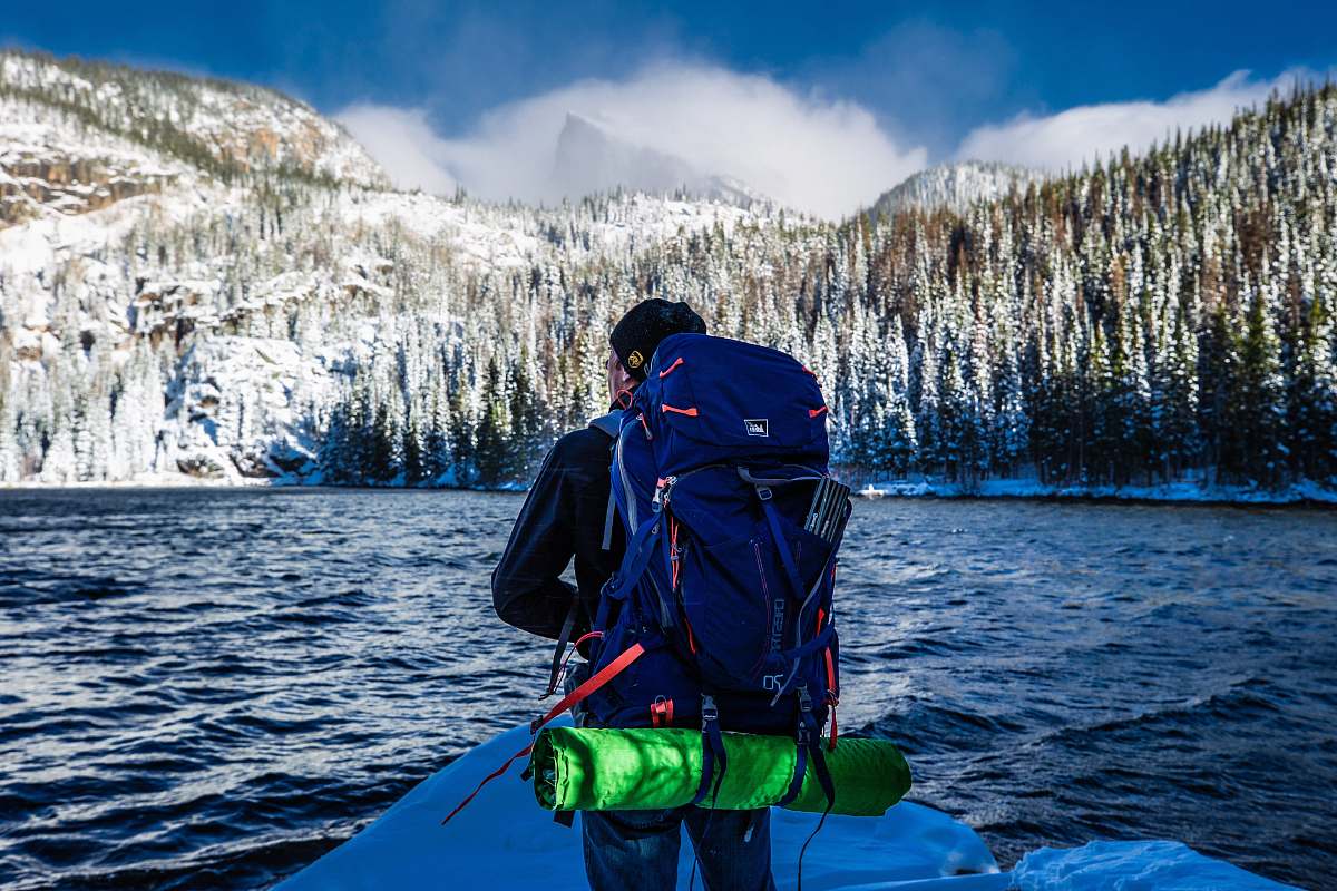 people man standing with blue hiking bag front of lake person