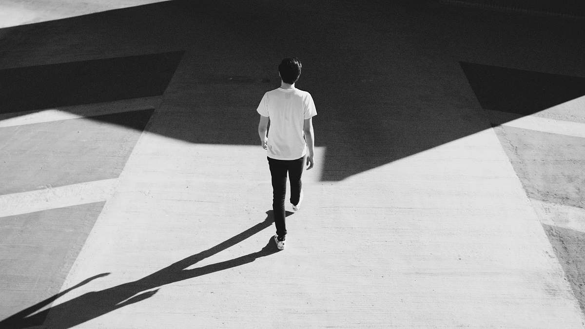 person man walking on gray concrete road black-and-white