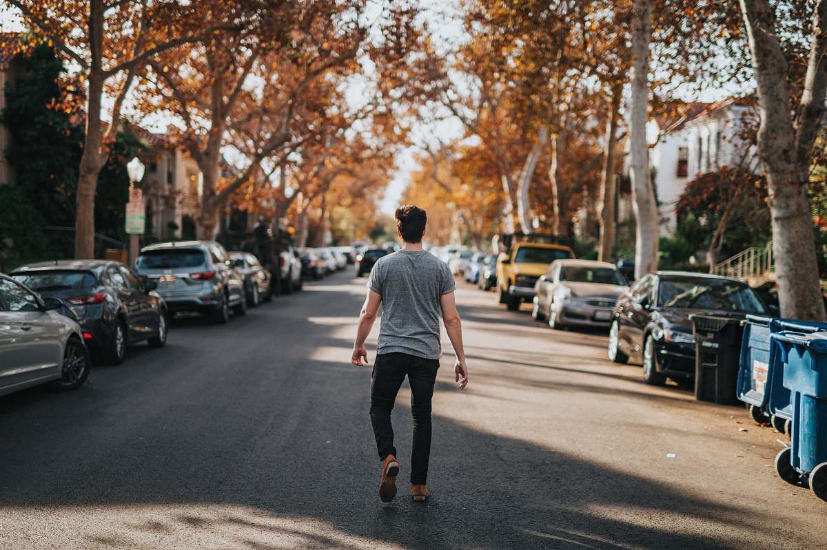 person man walking on road between parked vehicles people
