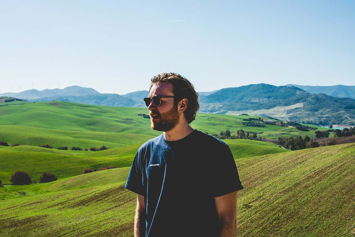 people man wearing black crew-neck t-shirt standing near hill at daytime person