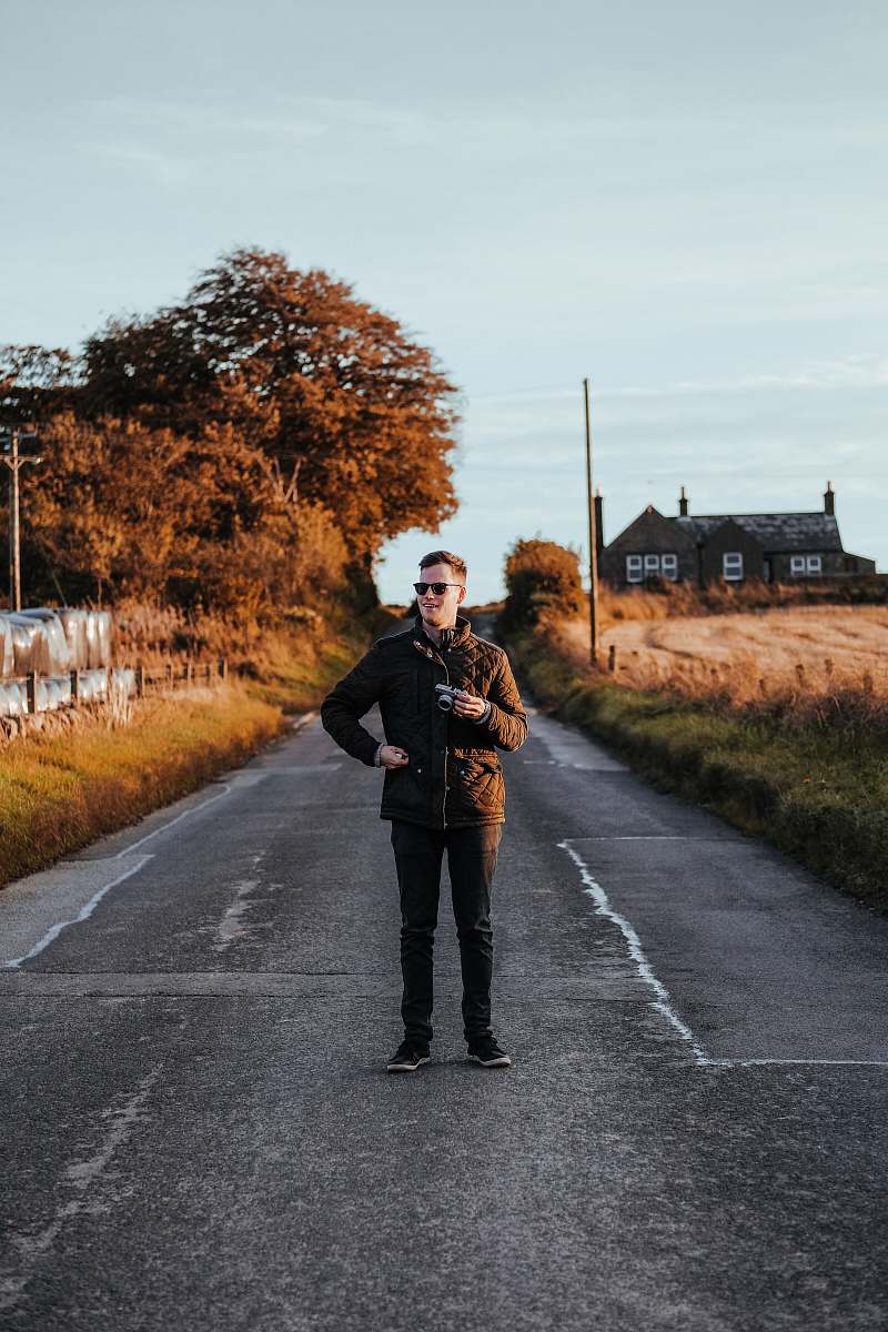 people man wearing brown zip-up jacket and black jeans standing on the center of a road person