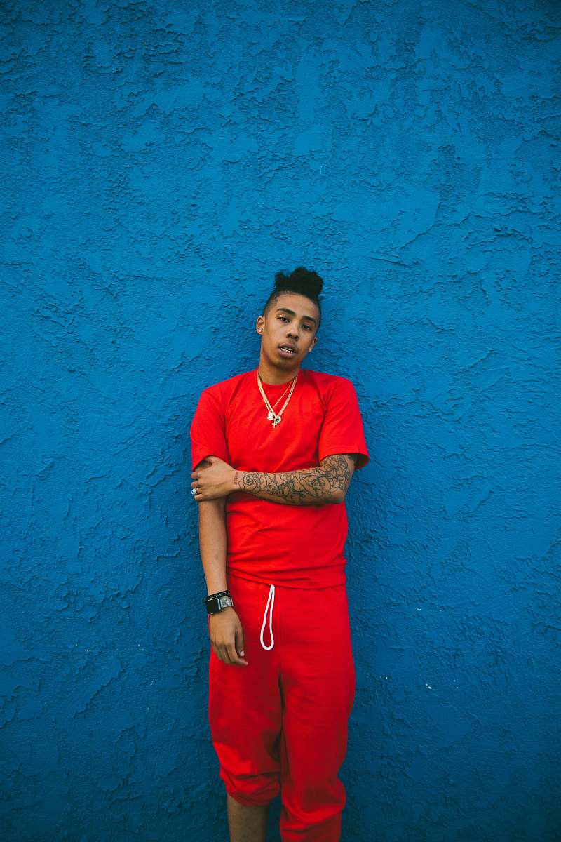people man wearing red crew-neck t-shirt and drawstring pants leaning on blue wall person