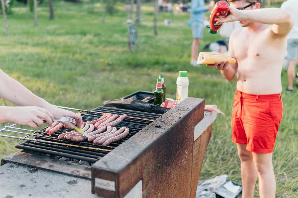 people man wearing red shorts standing at grill putting ketchup on hotdog bbq
