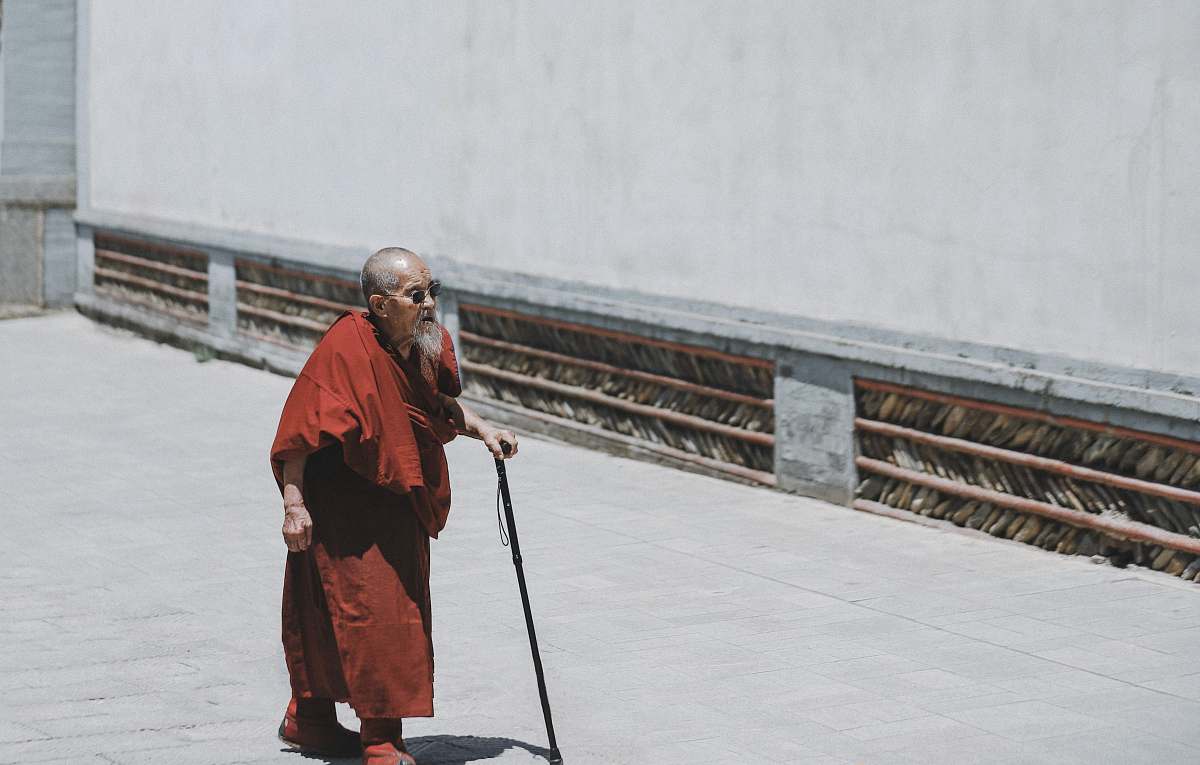 people monk walking while holding cane near white wall person