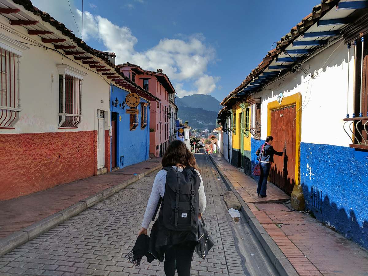 person person in gray shirt with backpack walking on street between houses people