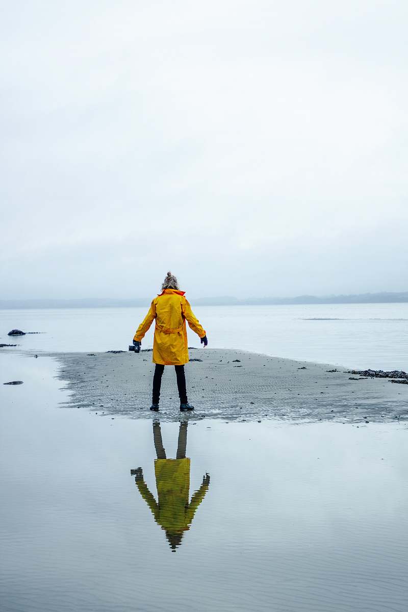 people person in yellow coat on gray sand surrounded by water person