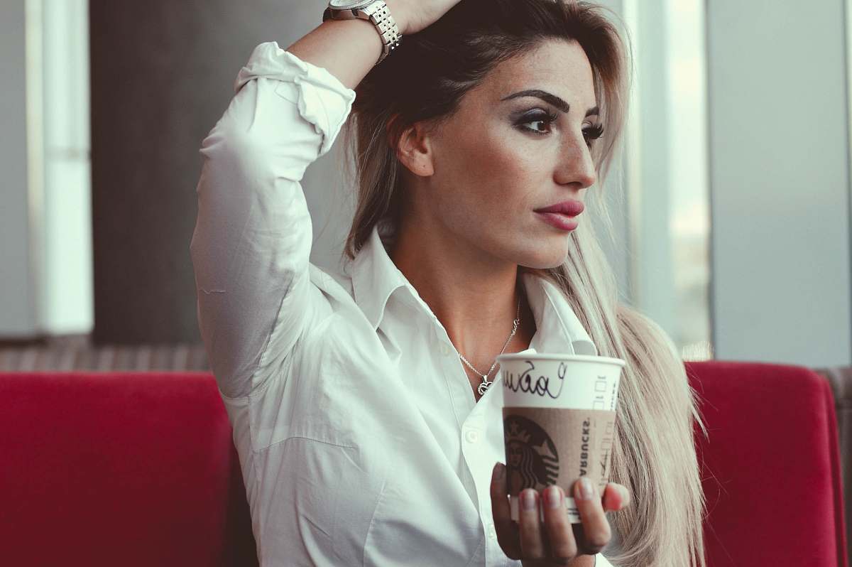 people selective focus photo of woman taking post while holding white disposable cup person