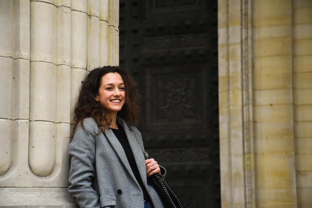 people smiling woman holding black shoulder bag leaning on white wall person