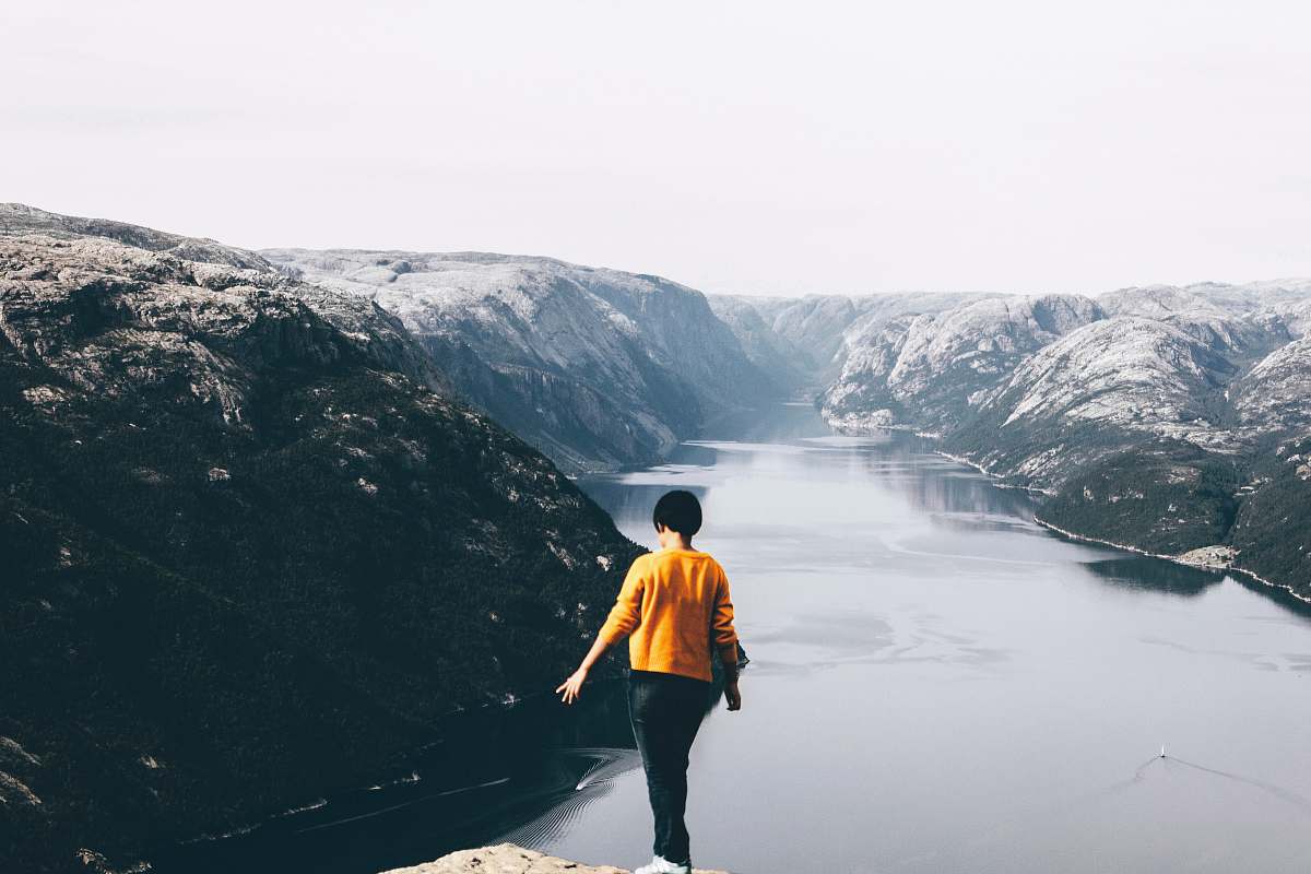 people standing woman on cliff with overlooking of mountain and body of water person