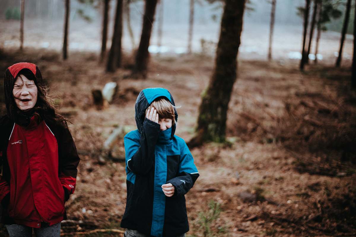 people two children wearing blue and red coats standing on woods person
