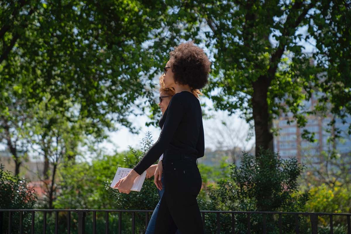 person two women walking near trees at daytime people