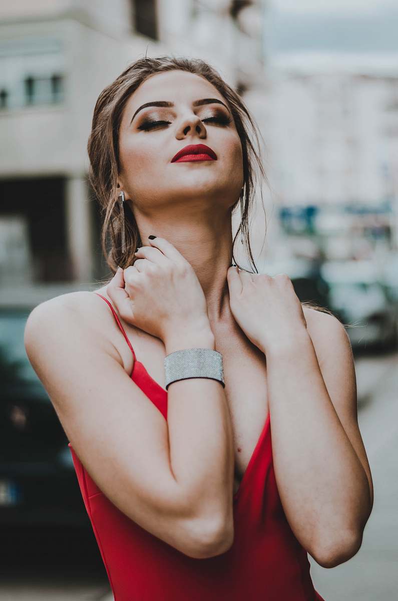 people woman holding her neck while closed eyes near building person