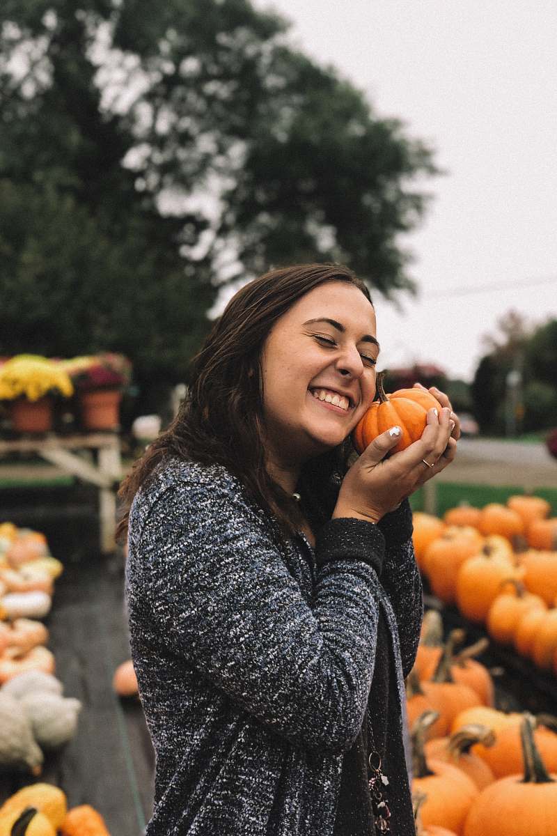 person woman holding orange pumpkin outside near green leafed tree under white sky during daytime people