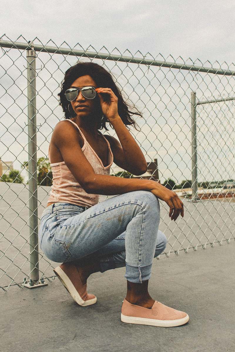 people woman holding sunglasses while kneeling beside cyclone fence person