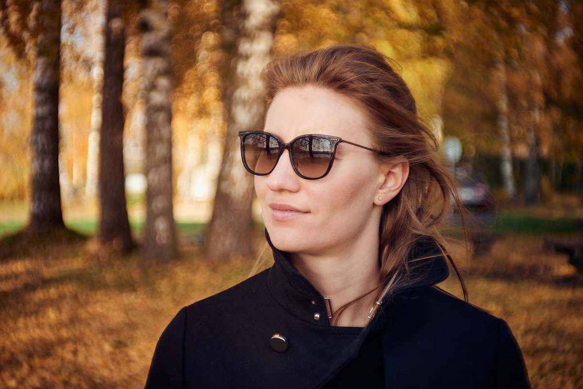 Capture the essence of urban elegance with this striking image of a woman dressed in a stylish black shirt and coat, confidently standing under the canopy of a vibrant tree. Perfect for lifestyle blogs, fashion articles, or marketing materials targeting contemporary audiences, this scene embodies a blend of nature and modern style that resonates with the chic and sophisticated.