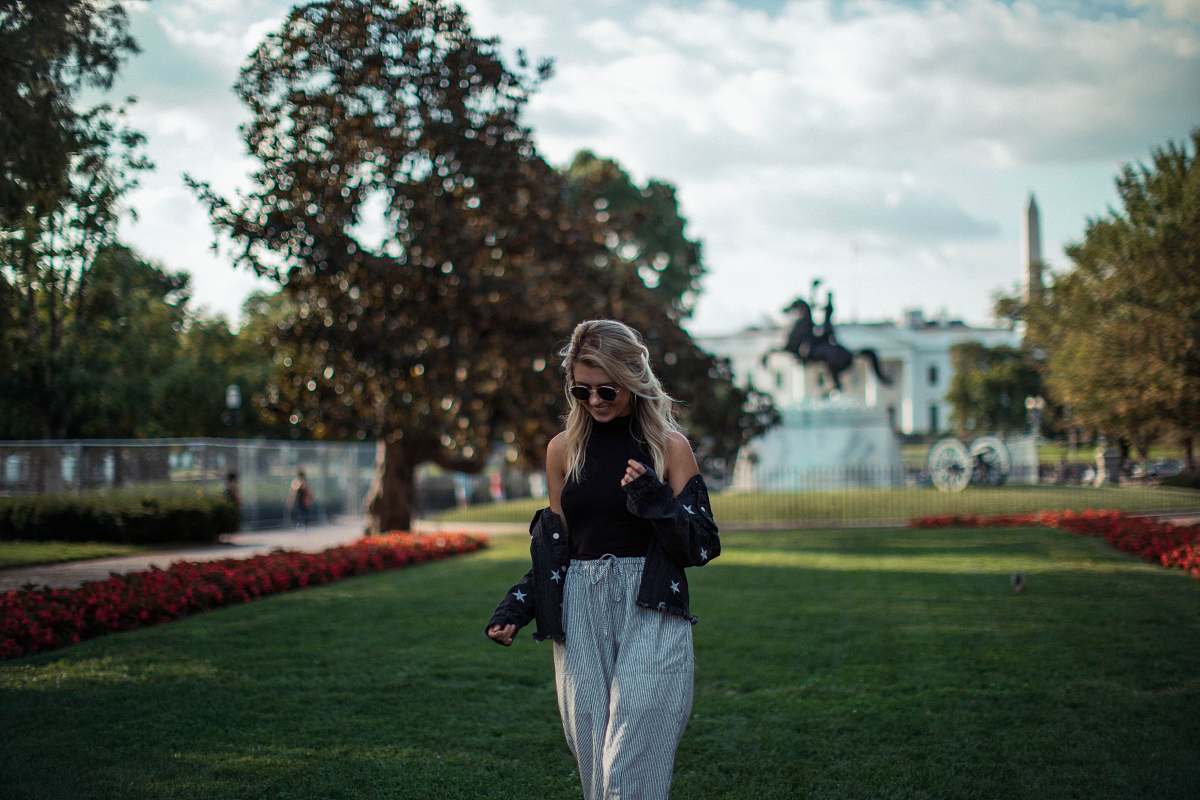 people woman in black top and white pants standing on green grass during daytime person