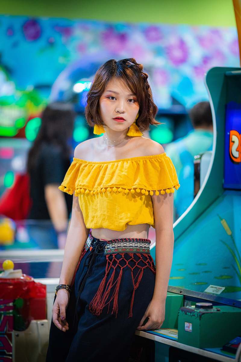 person woman in yellow off-shoulder crop top sitting on green and blue arcade machine people