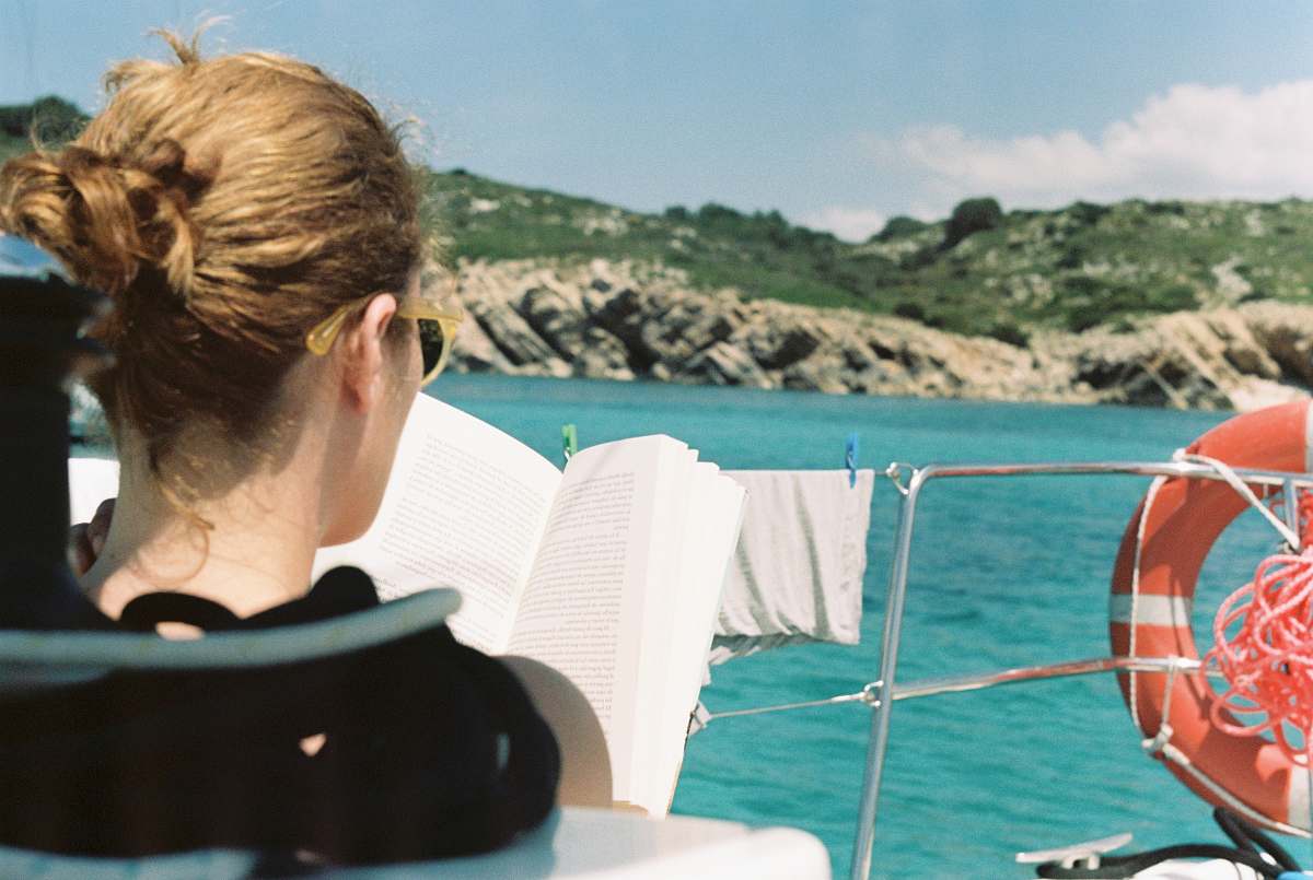This captivating image showcases a woman comfortably seated on a boat, deeply engrossed in her book. The serene surroundings and gentle ripples of the water create a peaceful atmosphere, perfect for capturing moments of relaxation and introspection. Ideal for use in lifestyle blogs, travel magazines, or promotional materials emphasizing leisure, reading, and nature.