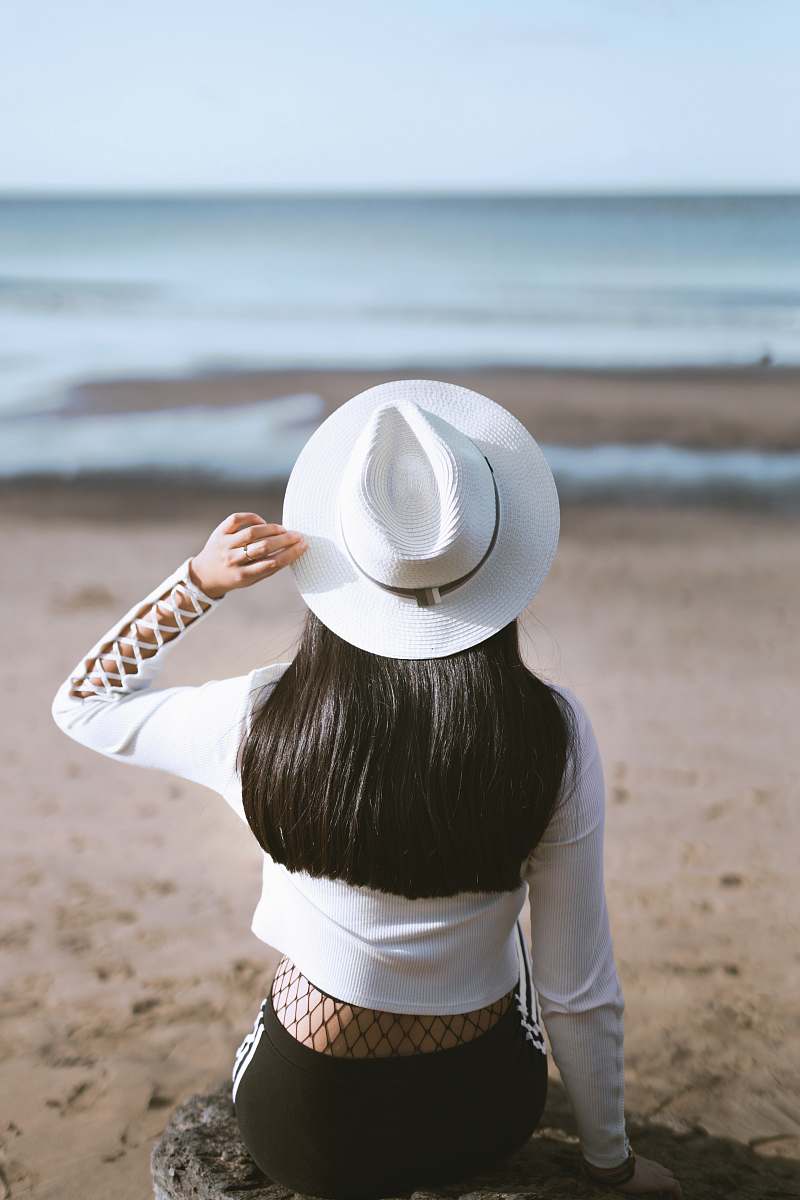 person woman sits on rock watching ocean hat