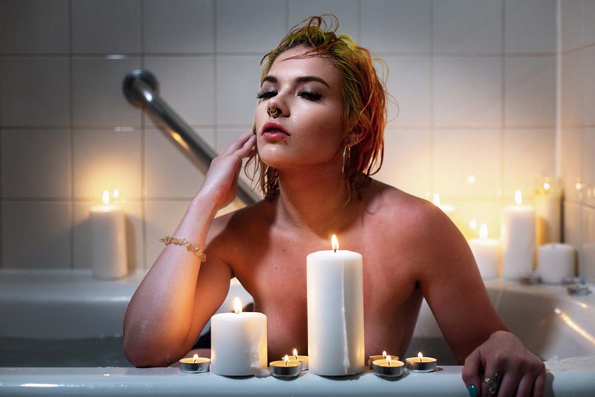 person woman sitting in bathtub behind lit tealight and pillar candles candle