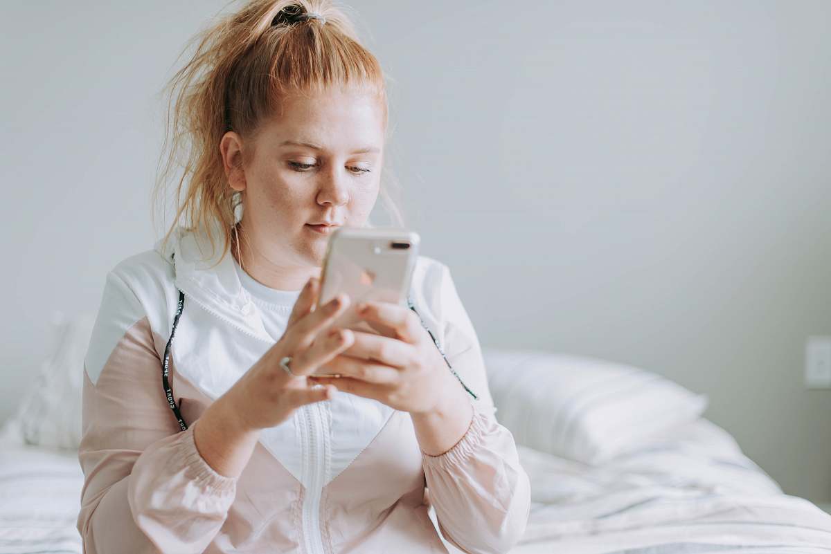 people woman sitting on bed while using gold turned 8 Plus person