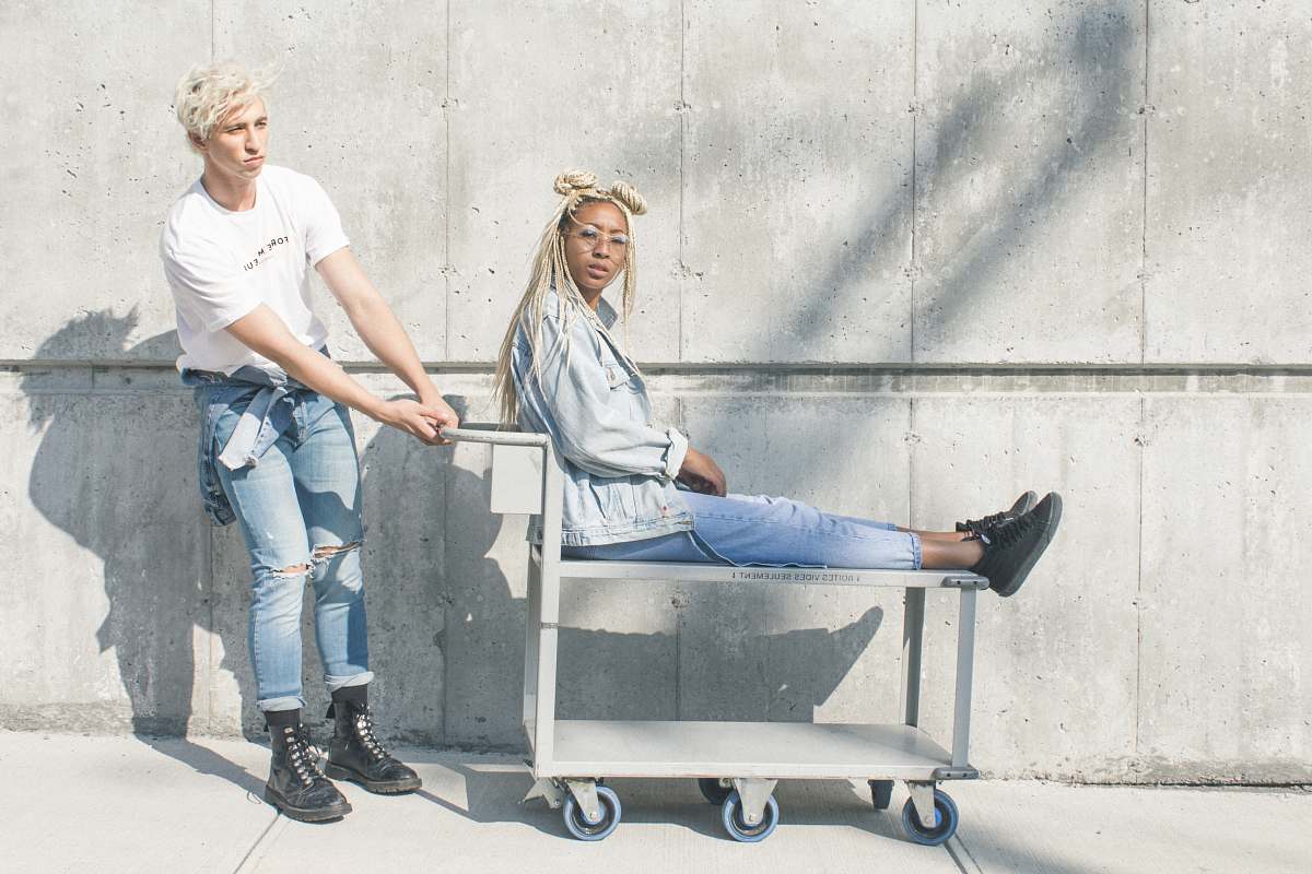 person woman sitting on serving cart while man holding push cart people