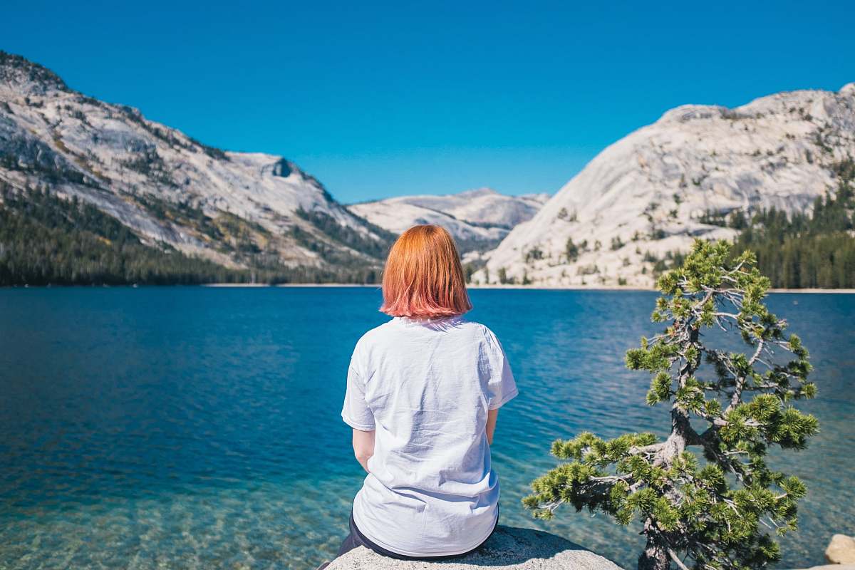 people woman sitting on the stone facing the ocean and mountain person