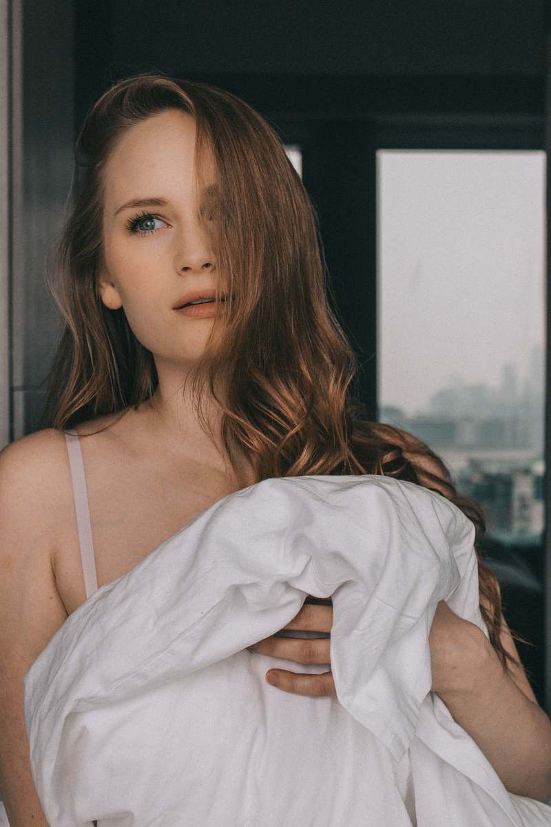person woman standing against the wall holding white blanket inside room people