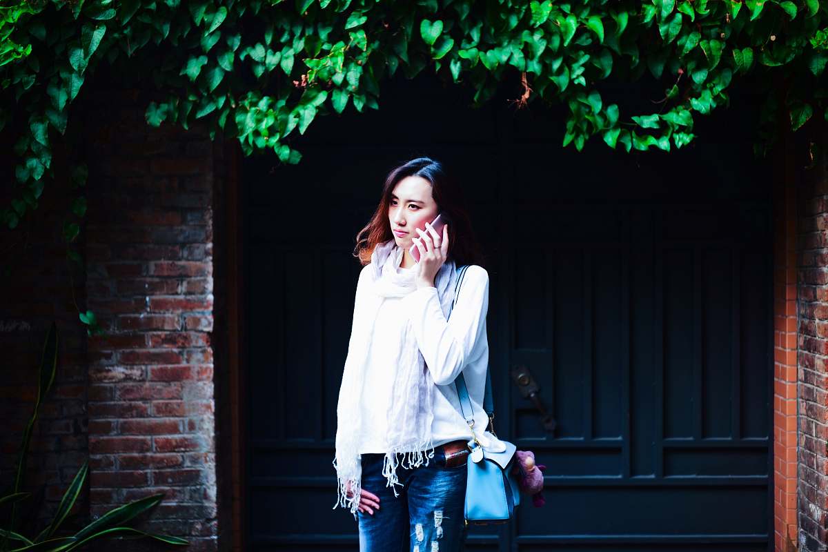 people woman standing behind gate while holding phone during daytime plant