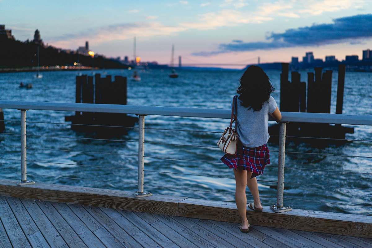person woman standing beside handrail overlooking body of water people
