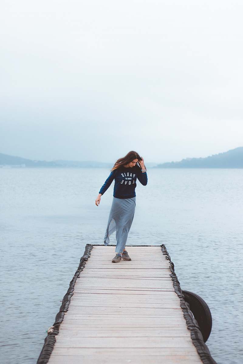 people woman standing in the middle of wooden footbridge leading to the sea person