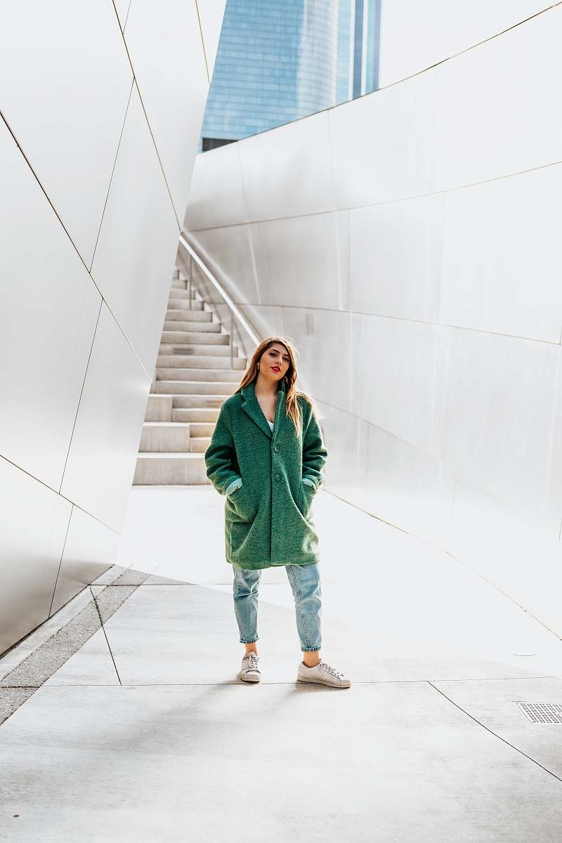 people woman standing near wall while hands in jacket pockets person