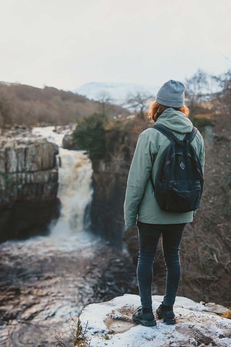 people woman standing on cliff facing waterfall person